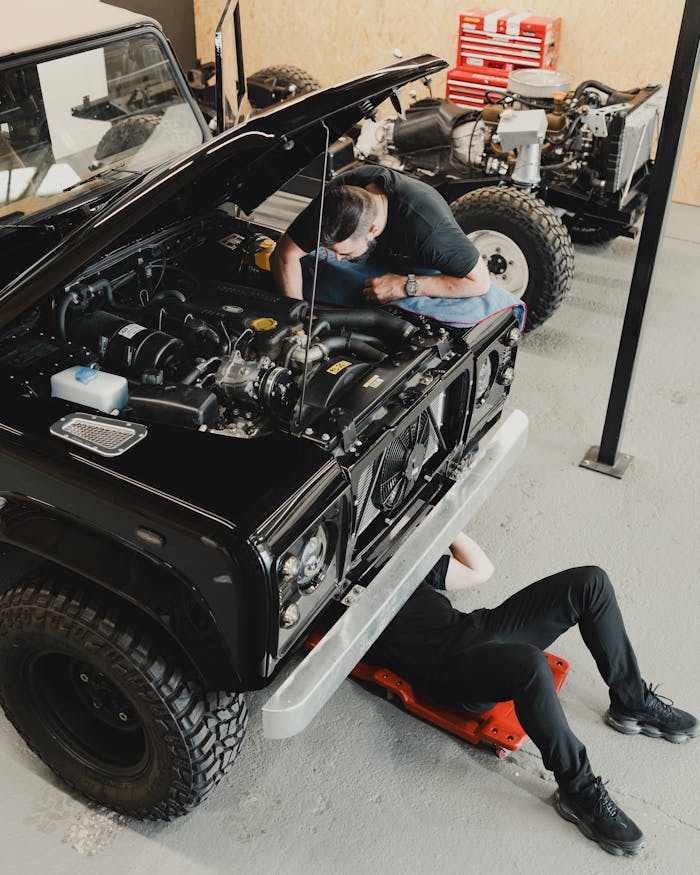 Two mechanics repairing a black off-road vehicle in a garage, focusing on engine work and maintenance.