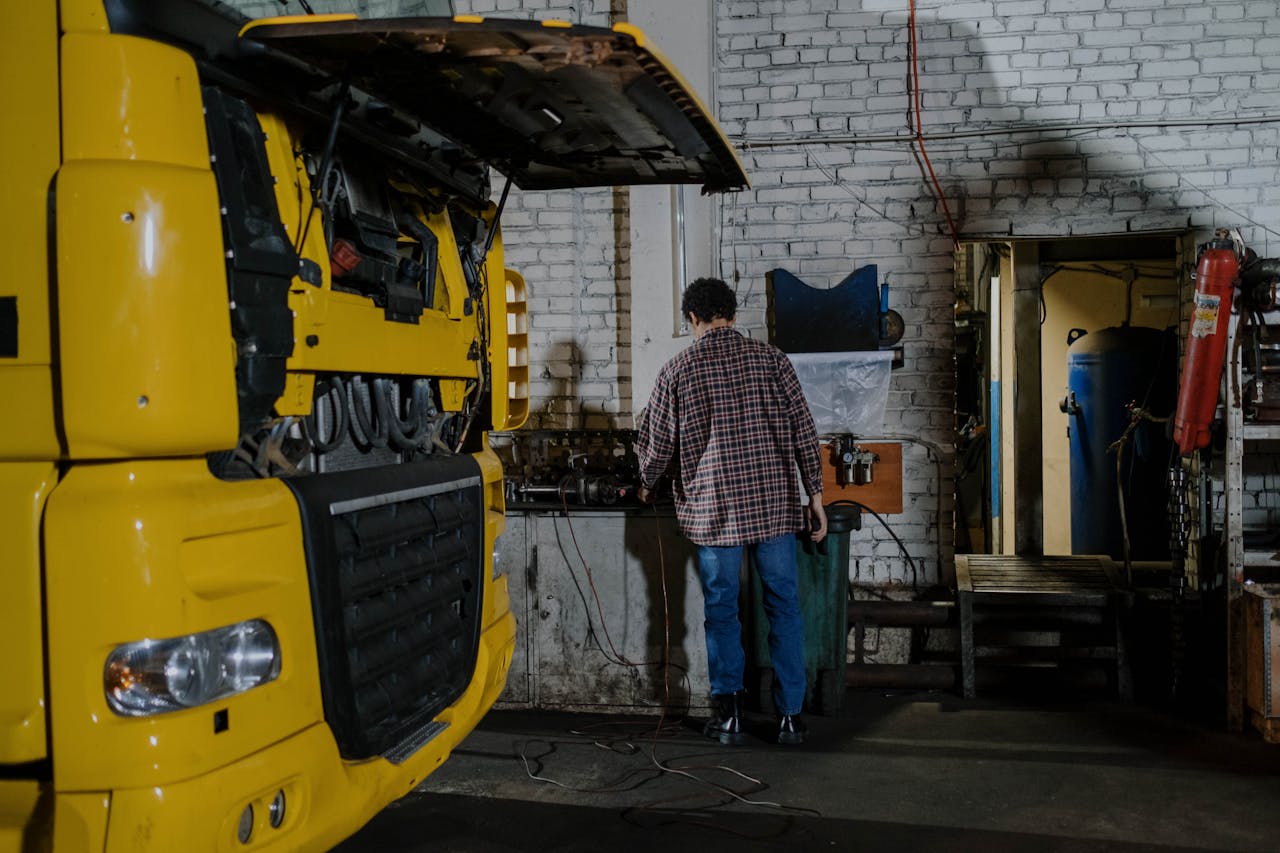 A mechanic working on a yellow truck engine in an indoor garage setting.
